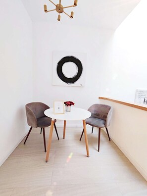 A small room with a round table, two chairs, a wall-mounted light fixture, and a black circular decoration.