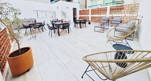 An outdoor seating area with tables and chairs, a potted plant, and a decorative wall.