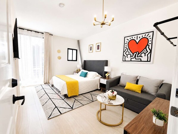 A modern hotel room with a bed, sofa, and a small table with flowers.