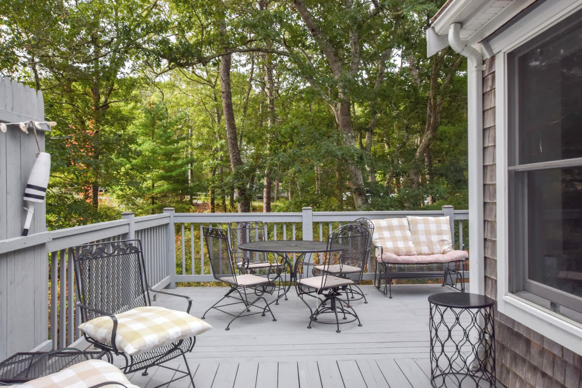 A covered outdoor deck with a table and chairs, surrounded by trees.