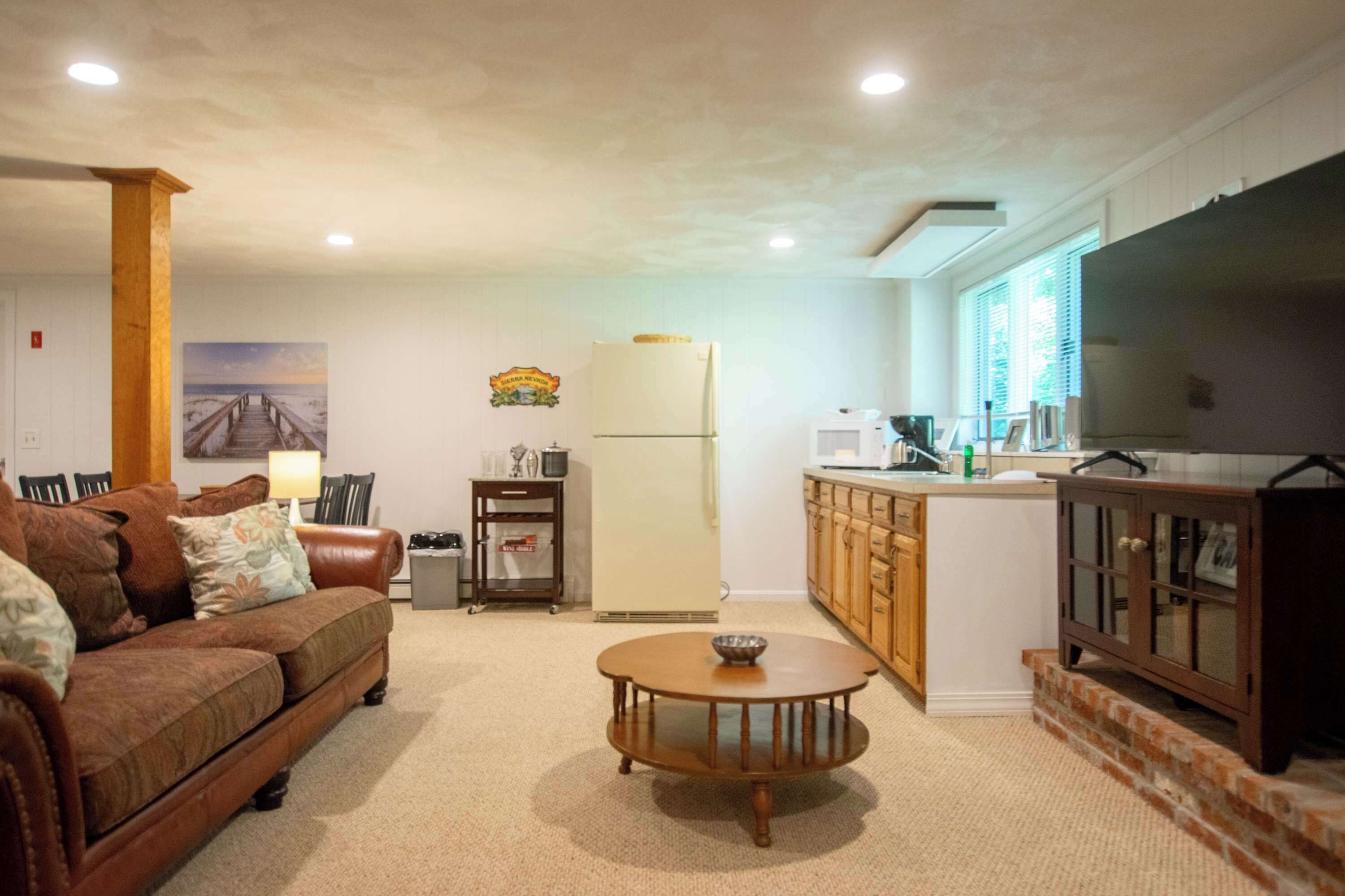 A living room with a brown sofa, a wooden coffee table, and a kitchen area with wooden cabinets and a refrigerator.