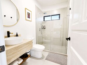 Casa de banho moderna com lavatório branco, sanita e cabine de duche em vidro.