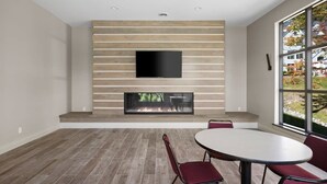 Un soggiorno moderno con camino, una TV a schermo piatto montata su una parete in legno e un'area pranzo con tavolo rotondo e sedie rosse.