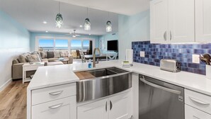 Une cuisine moderne dotée d’un grand îlot central, d’appareils électroménagers en acier inoxydable et offrant une vue sur l’extérieur.