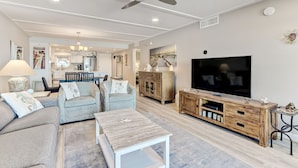 A modern living room with a sofa, coffee table, TV, and wooden entertainment unit. - Sunrise View | Oceanfront Condo Amelia South D6 on Amelia Island! (Fernandina Beach)
