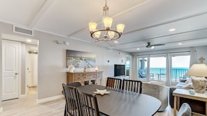 A modern dining area with a chandelier, a dining table, and chairs. There is a view of the ocean through large windows. - Sunrise View | Oceanfront Condo Amelia South D6 on Amelia Island! (Fernandina Beach)