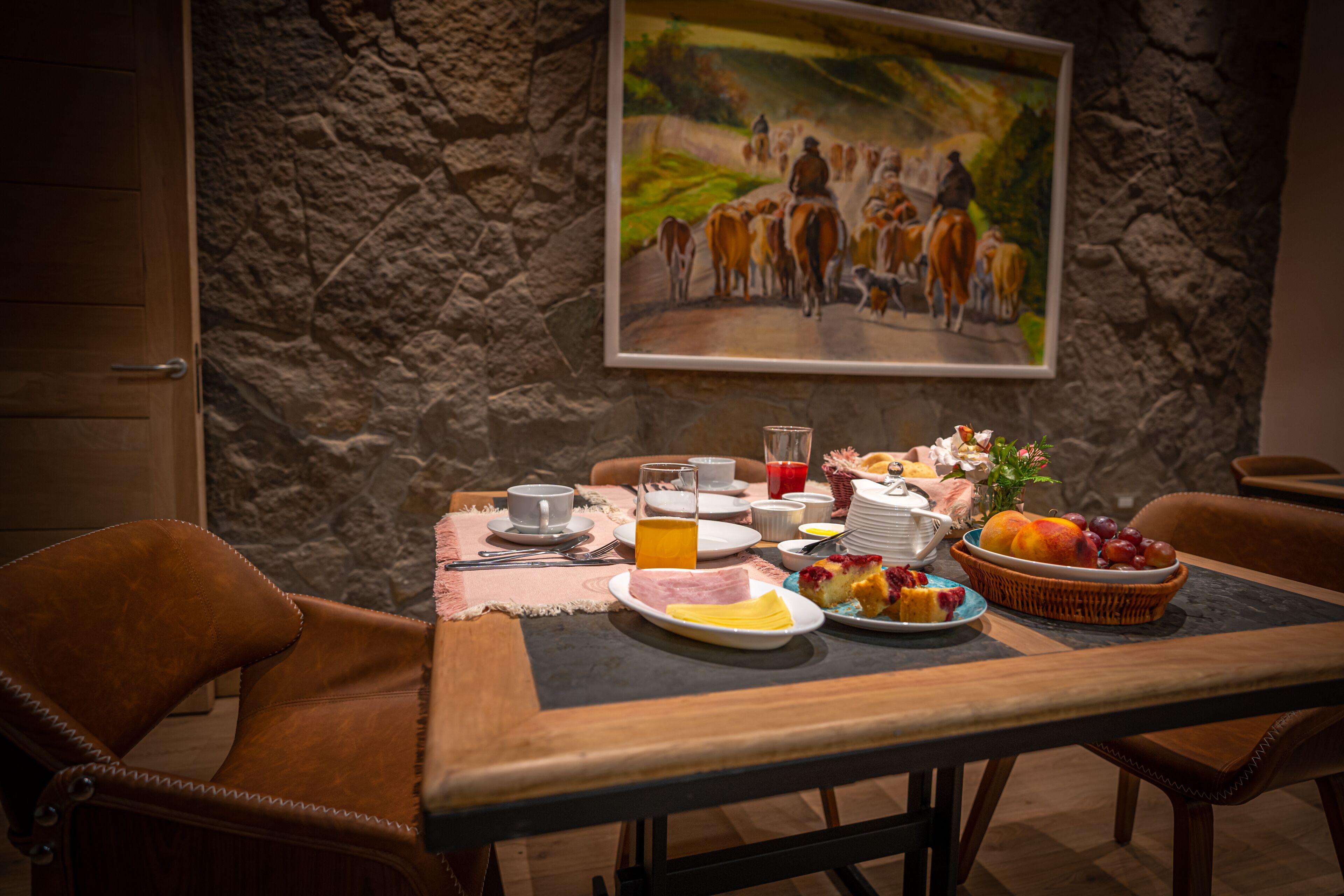 A dining table set with breakfast items, a painting on the wall, and stone-textured walls.
