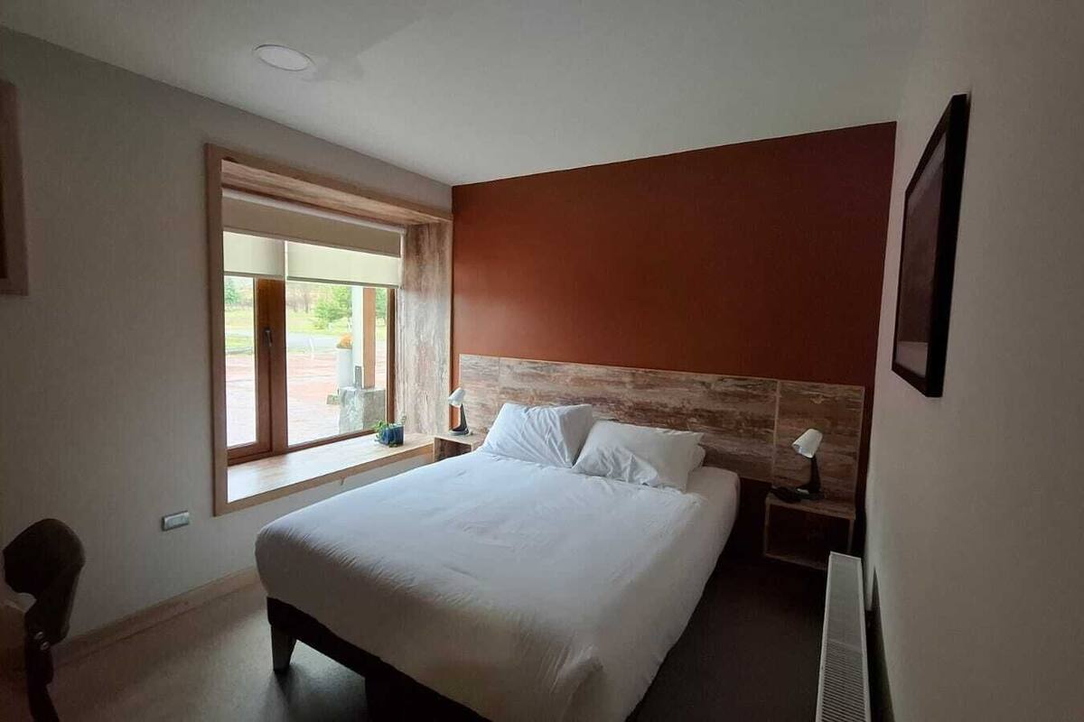 Ein Schlafzimmer mit einem großen Bett, einem Nachttisch, einem Fenster und Blick ins Freie.