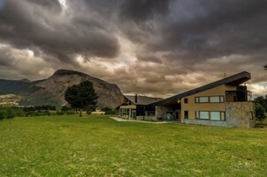 A modern house with a large mountain in the background, a grassy yard, and a cloudy sky.