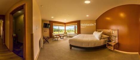 A bedroom with a bed, a desk, and a chair. There is a window with a view of the outdoors.