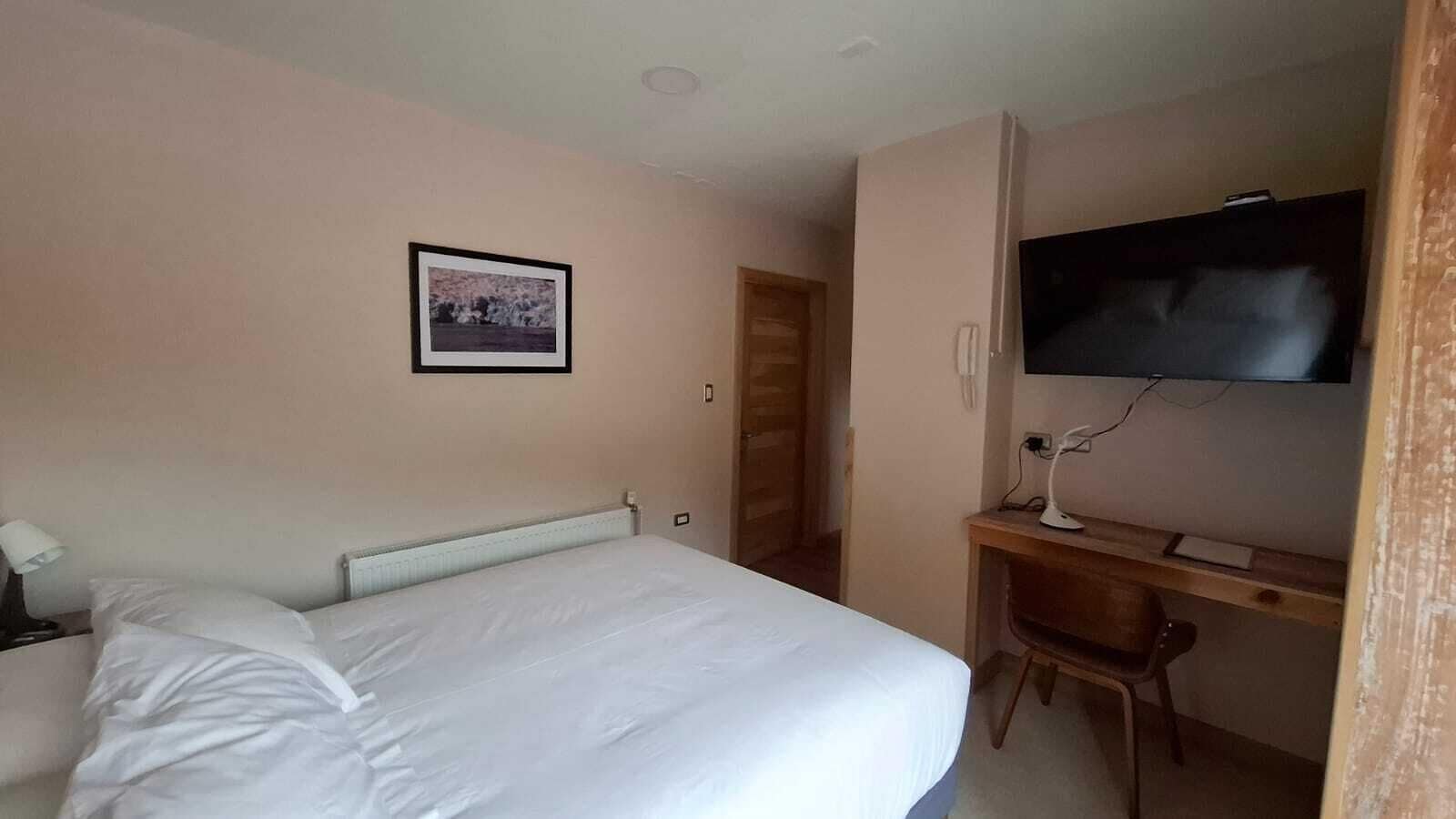 A hotel room with a bed, a desk with a computer, a TV, and a framed picture on the wall.