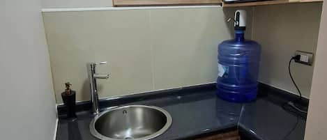A compact kitchen with a built-in sink, a window, a microwave, and a water dispenser.