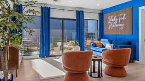 Un salon moderne avec un canapé bleu, des fauteuils orange et un panneau lumineux néon.