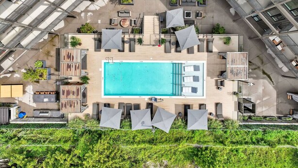 Vue aérienne d’un espace piscine sur le toit, avec plusieurs chaises longues, des parasols et une piscine.