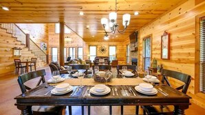 Un interior de madera con una mesa de comedor preparada para seis comensales, una escalera y una araña.