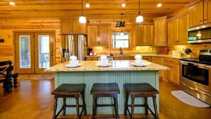 Interior de una cabaña de madera con cocina, que incluye una isla central, taburetes de bar y electrodomésticos empotrados.