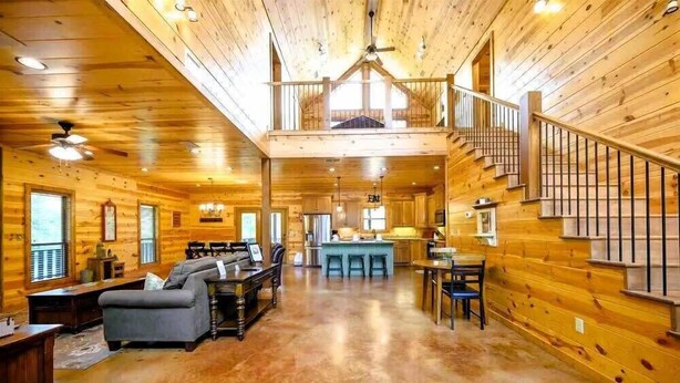Interior espacioso de una cabaña de troncos, con sala de estar, comedor y una escalera que conduce a un nivel superior.