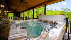 Un jacuzzi en un espacio exterior cubierto con vigas de madera, vistas a la vegetación y una terraza con sillas.