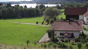 A rural house with a red-tiled roof, a paved driveway, and a view of a lake. - Gemütliches Familien Ferienhaus in Ruhiger Umgebung m. Großer Terrasse u. Balkon (Steingaden)