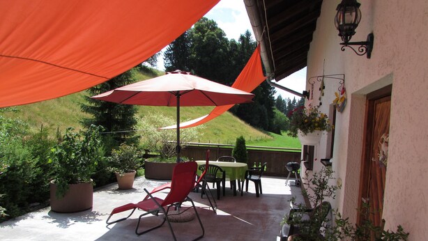 A patio with a table and chairs, a red umbrella, and potted plants. - Gemütliches Familien Ferienhaus in Ruhiger Umgebung m. Großer Terrasse u. Balkon (Steingaden)