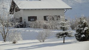 A snow-covered house with a sloped roof, a chimney, and a small porch area. - Gemütliches Familien Ferienhaus in Ruhiger Umgebung m. Großer Terrasse u. Balkon (Steingaden)
