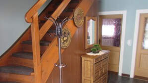 A wooden staircase with a metal coat rack and decorative plates, a wooden cabinet, and a striped rug. - Gemütliches Familien Ferienhaus in Ruhiger Umgebung m. Großer Terrasse u. Balkon (Steingaden)