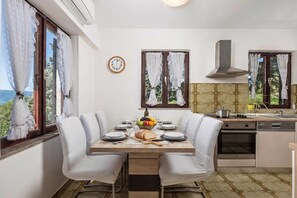 A dining area with a table set for two, a clock on the wall, and a view of the outdoors. - Family House Rose With Pool (Krk)