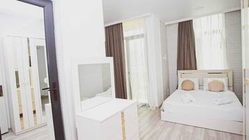 A hotel room with a white bed, a dresser with a mirror, and a wardrobe with glass doors.