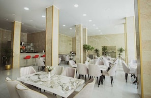 Experience the elegant lobby with a marble reception desk, seating areas, and a dining space surrounded by lush greenery.