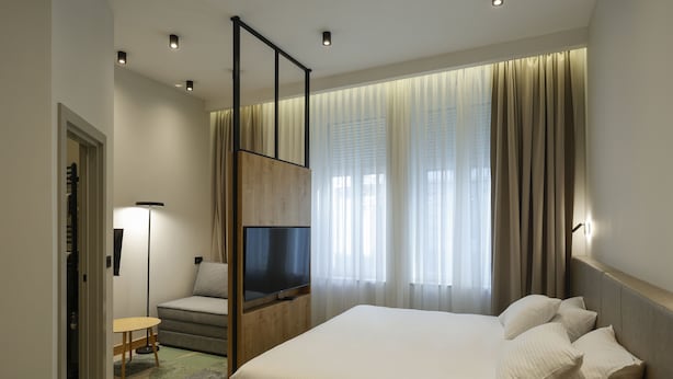 A modern hotel room with a large bed, a TV, a sofa, and a small table. - Hop Inn Rooms & Suites Belgrade (Belgrade)