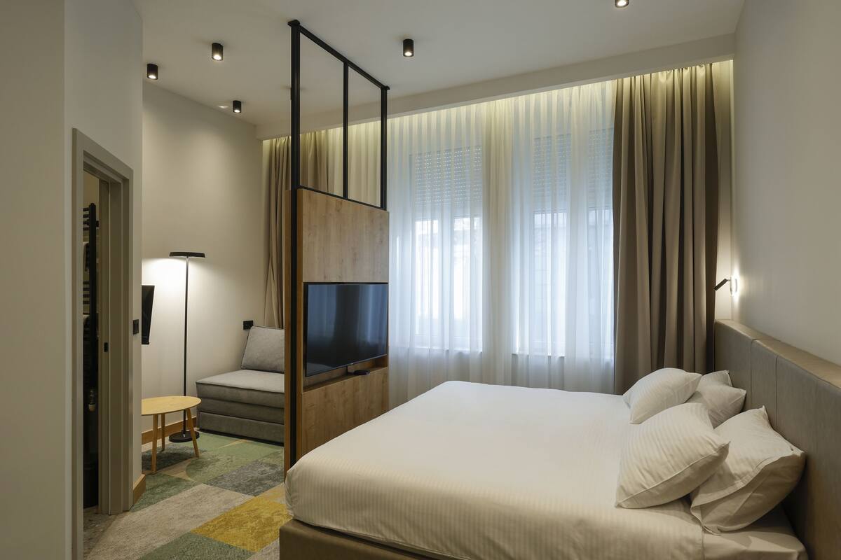 A modern hotel room with a large bed, a TV, a sofa, and a small table.
