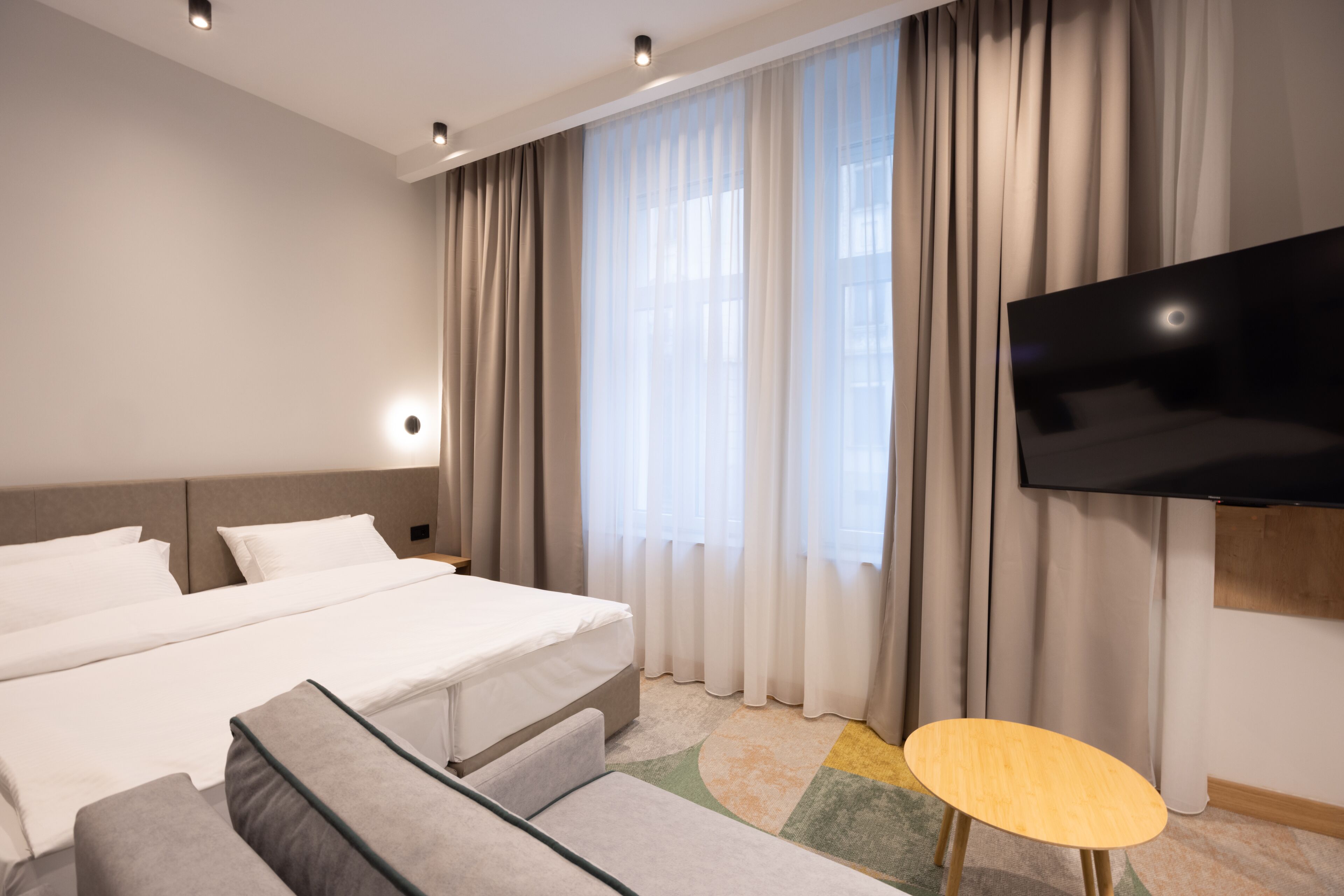 Une chambre d’hôtel moderne avec un grand lit, un canapé, une petite table et un téléviseur fixé au mur.