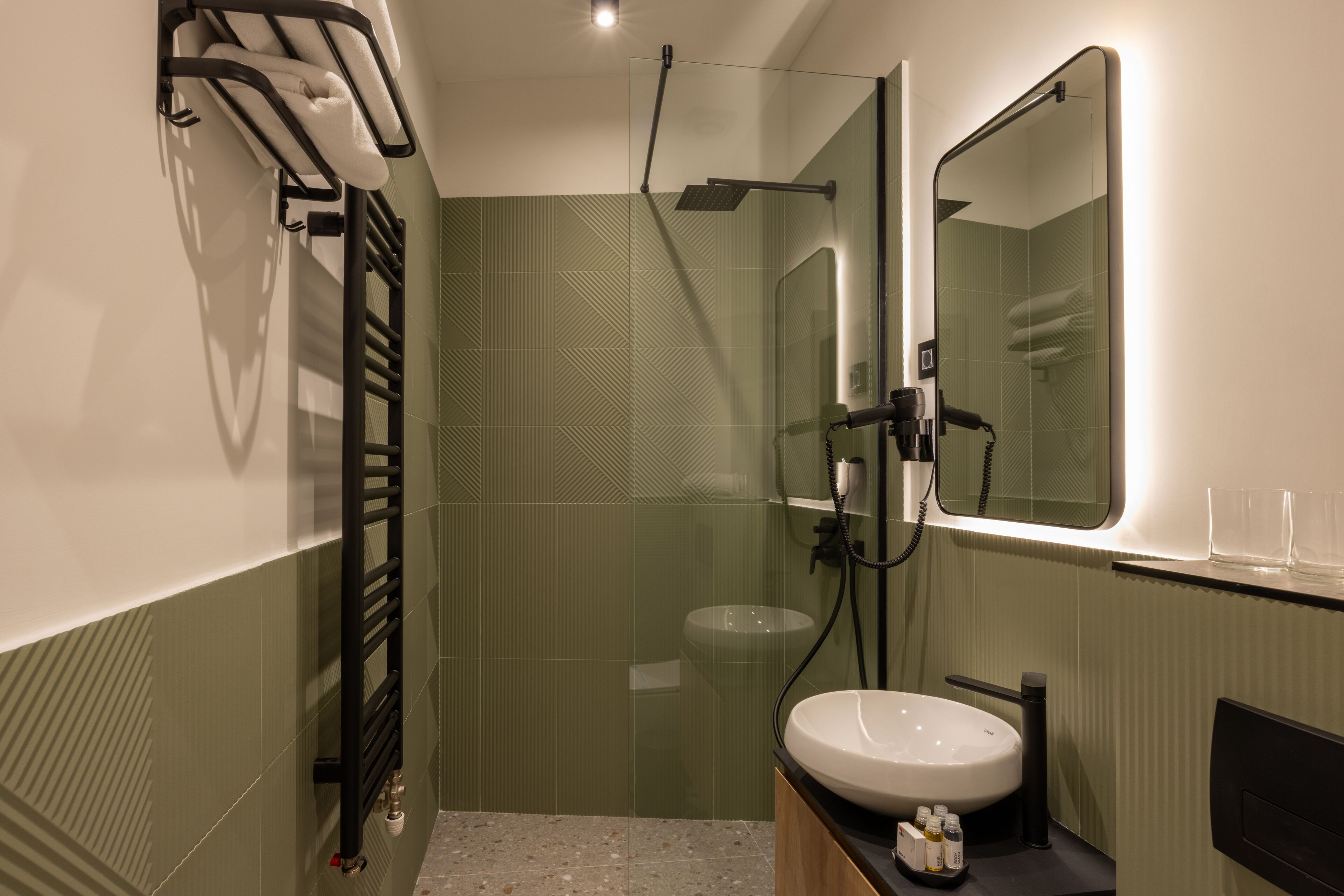 A modern bathroom with a glass shower enclosure, a white sink, and a towel rack.