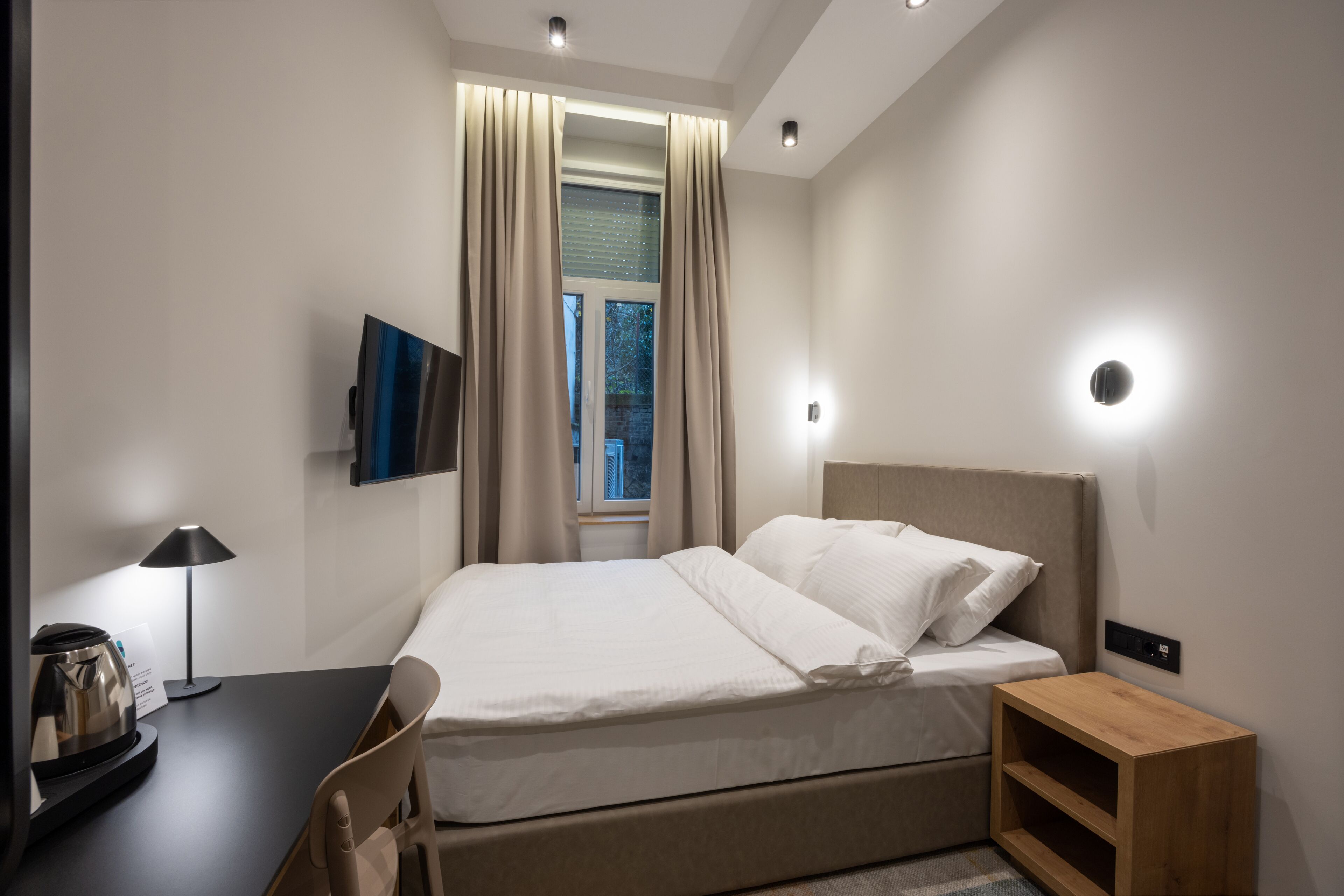 Une chambre d’hôtel moderne équipée d’un lit, d’un bureau avec une lampe, d’une télévision et d’une fenêtre avec des rideaux.
