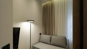 A modern room with a grey sofa, a floor lamp, and a window with curtains. - Hop Inn Rooms & Suites Belgrade (Belgrade)