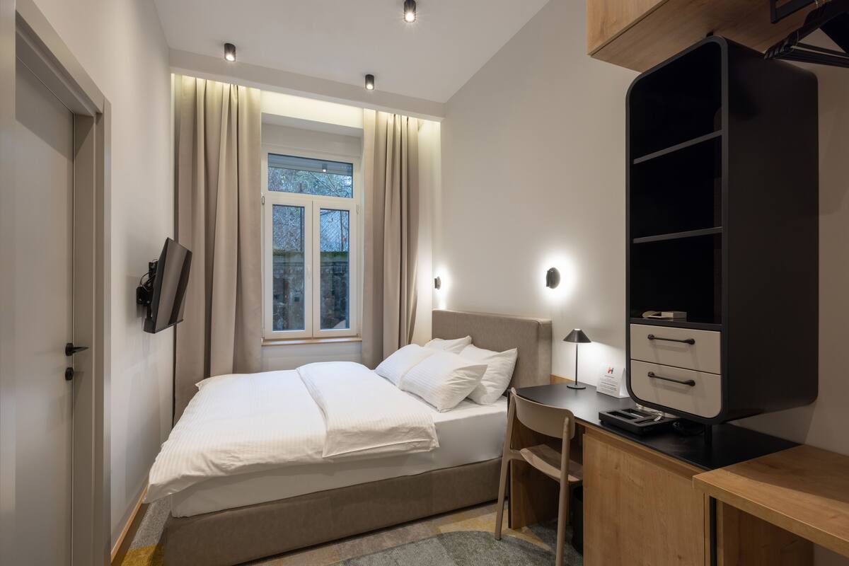 A modern bedroom with a bed, bedside table, desk, and wardrobe.