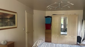 A bedroom with a bed, a wardrobe, a dresser, a painting, and a ceiling light fixture.