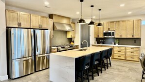 A modern kitchen with stainless steel appliances, wooden cabinets, and a marble island with bar stools.