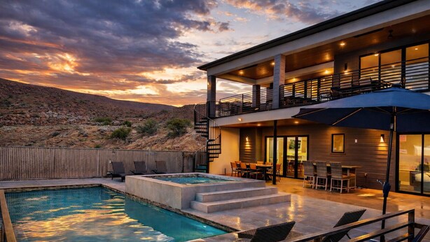 A modern outdoor pool area with a two-story building, a covered seating area, and a view of a desert landscape.