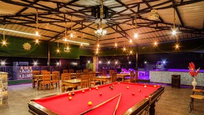 A billiards room with a pool table, chairs, and tables, under a high ceiling with exposed beams and hanging lights. - HOTEL VINSOBER PRIDE INN (Narendranagar)