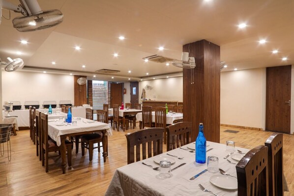 A dining area with multiple tables and chairs, ceiling lights, and a wooden column.