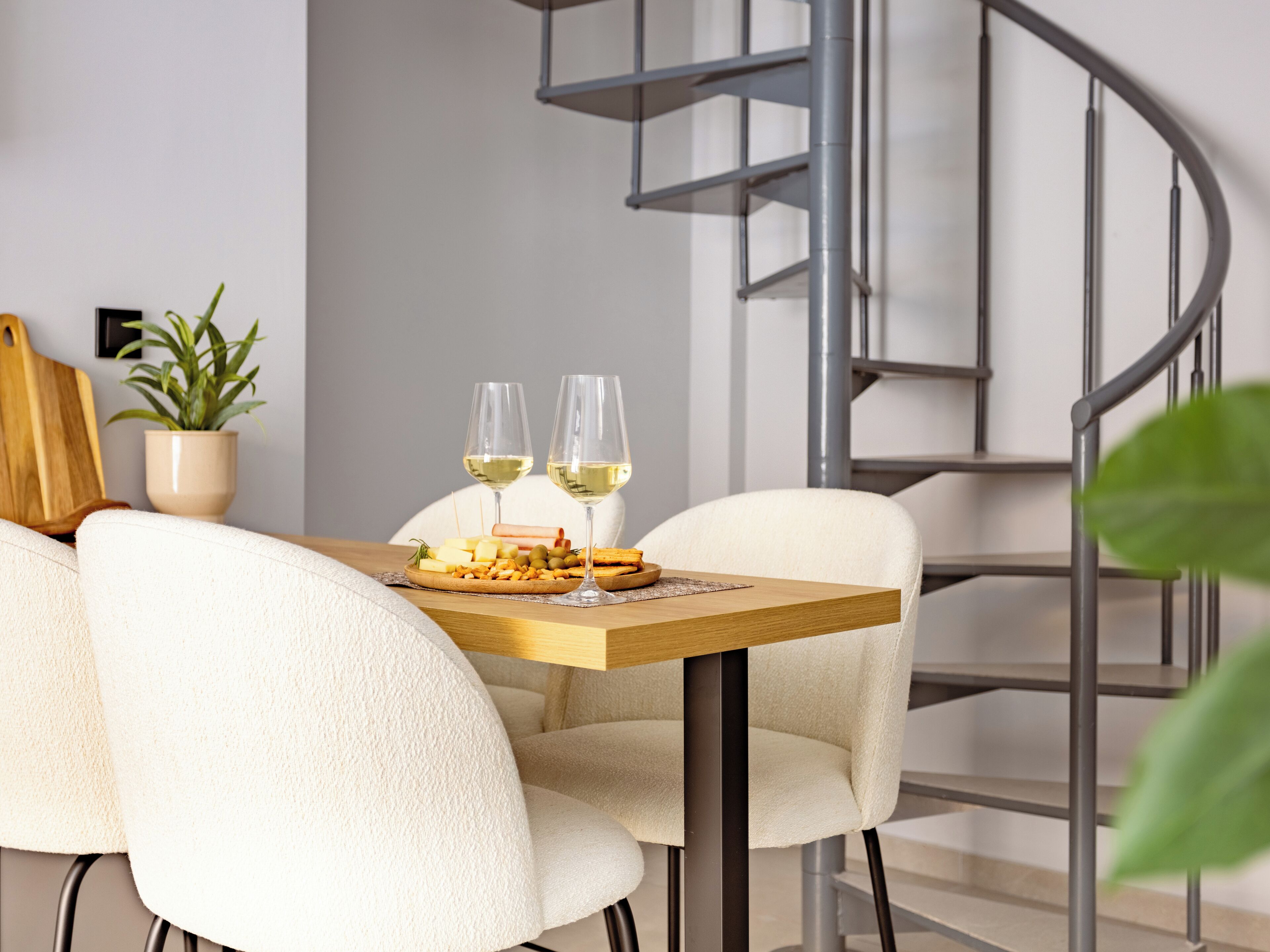 A modern dining area with a wooden table, white chairs, and a spiral staircase in the background.