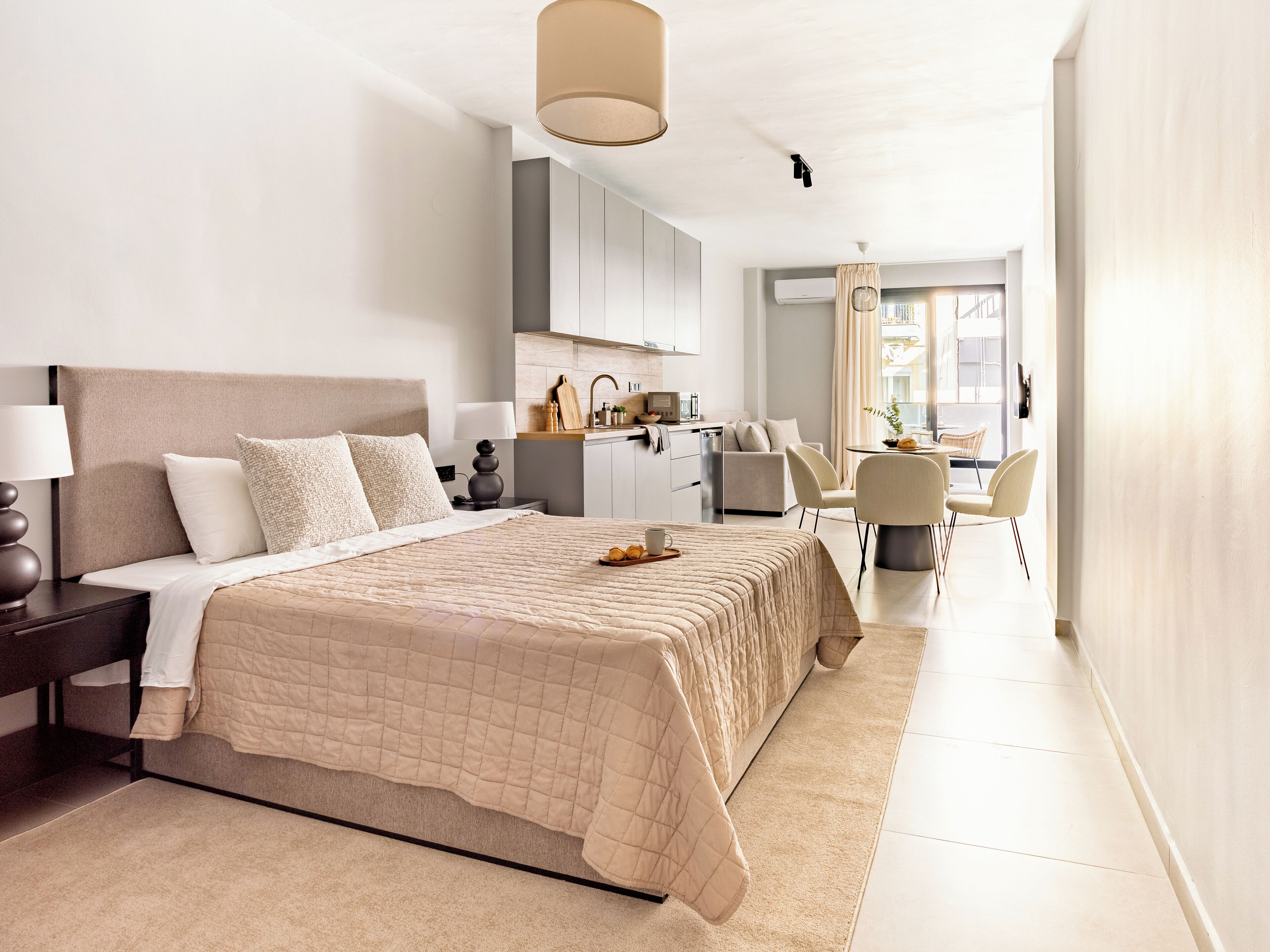 A modern hotel room with a large bed, a desk, and a kitchenette.
