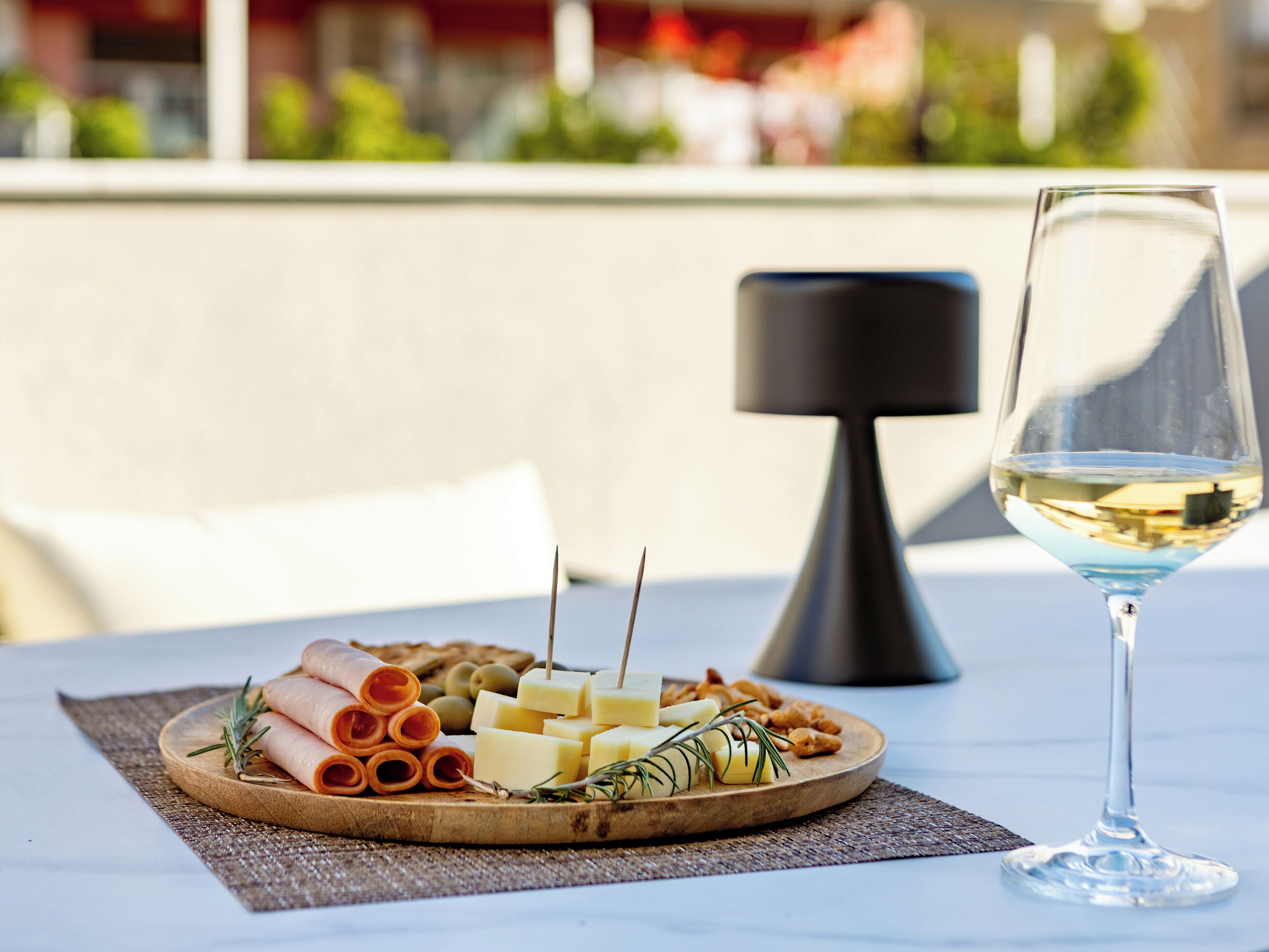 Une table avec une planche de charcuterie, un verre de vin blanc et une lampe moderne.
