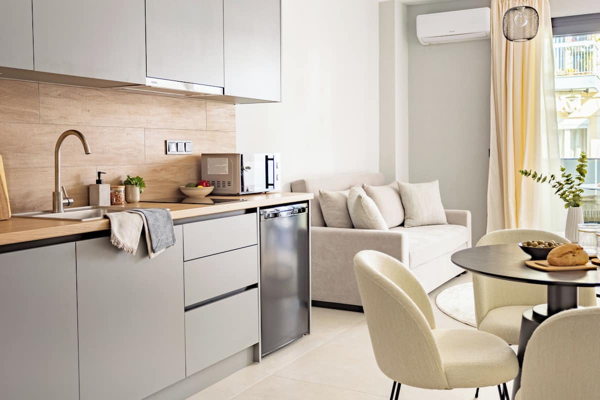 Una cocina moderna con lavavajillas incorporado, microondas y un lavabo con grifo. Hay una zona de comedor con una mesa redonda y sillas, y un sofá al fondo.