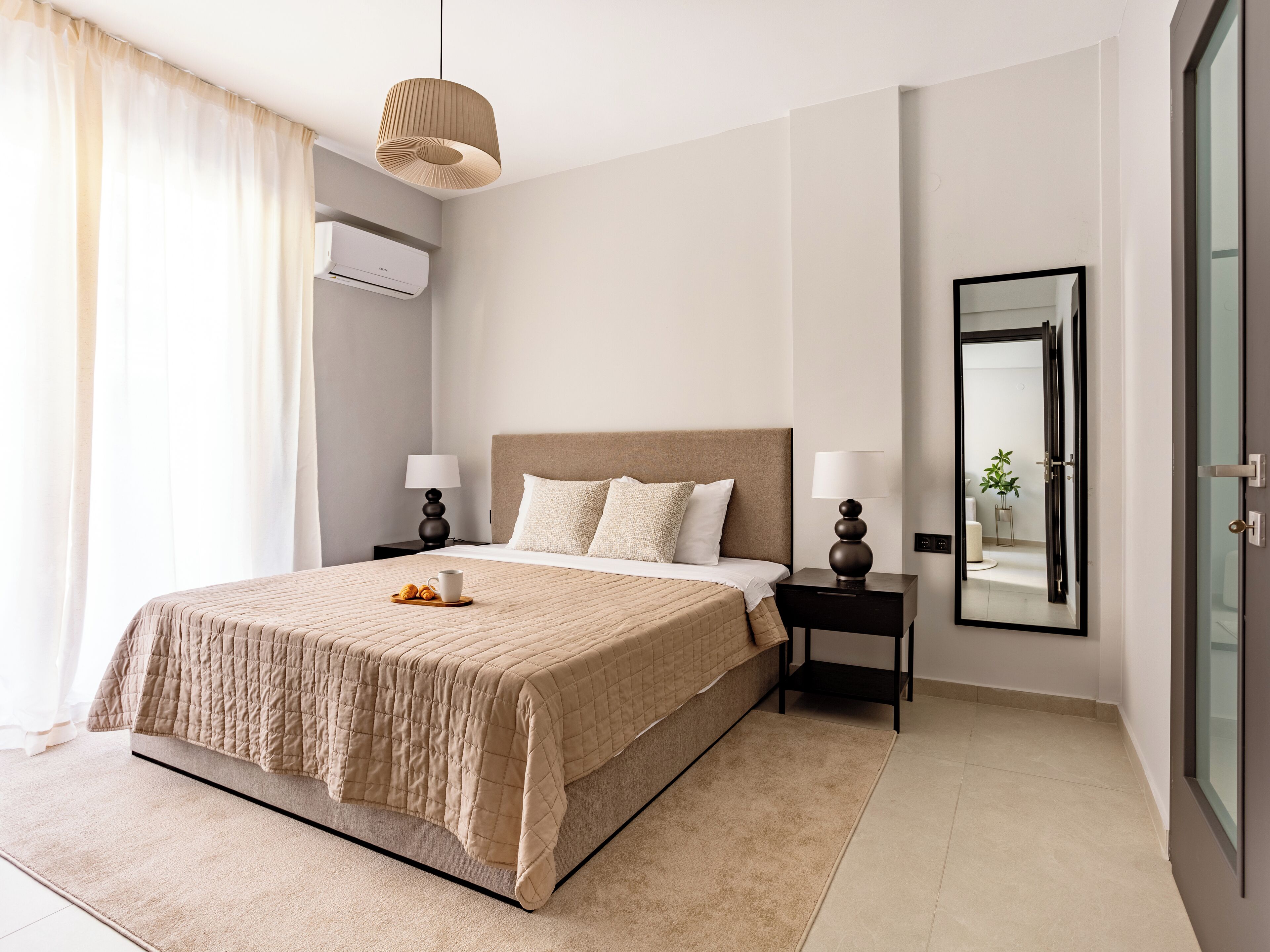 Une chambre d’hôtel moderne avec un grand lit, deux tables de chevet avec des lampes, un miroir et une vue sur la salle de bain.