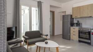 Un salon moderne avec un canapé gris, une table basse blanche et un téléviseur. L’espace cuisine comprend un réfrigérateur, un four à micro-ondes et un four traditionnel.