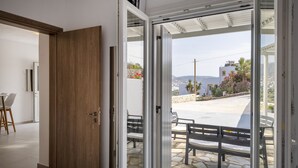 Une pièce moderne avec une porte en bois, une porte vitrée donnant sur un patio extérieur doté d’un sol en pierre et d’un banc en métal.