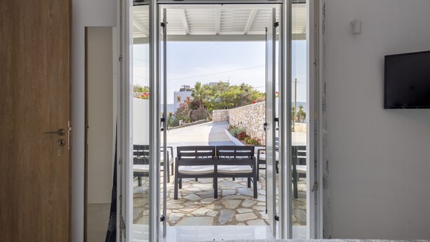 Une porte ouverte donne sur un patio doté d’un sol en pierre, d’un banc et d’un téléviseur fixé au mur.