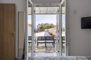 An open door leading to a patio with a stone floor, a bench, and a TV mounted on the wall. - Cycladic Sunlight 2bedroom House (Paros)